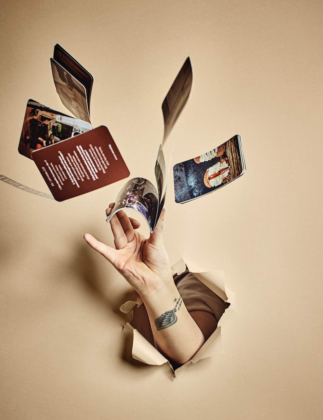 Main surgissant d'un fond beige et lançant des cartes illustrées, photo créative de produit