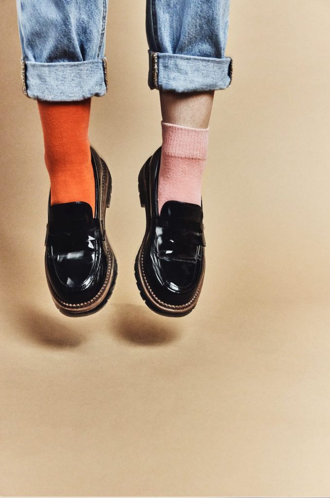 Pieds en mocassins vernis et chaussettes colorées sur fond beige, photo décalée en studio