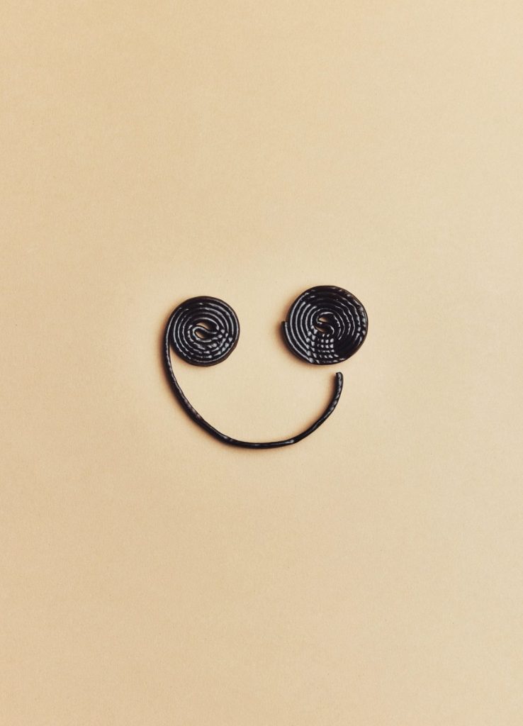 Smiley dessiné avec deux rouleaux de réglisse sur fond beige, nature morte créative